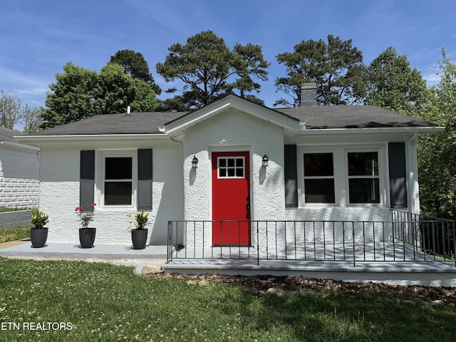 bungalow-style house with a front yard, stucco siding, and a chimney