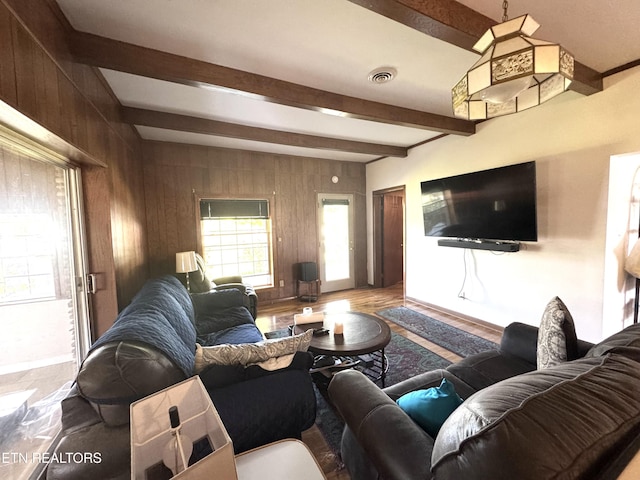 living area with wooden walls, baseboards, beamed ceiling, and visible vents