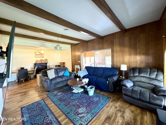 living room featuring a ceiling fan, a fireplace, wood walls, wood finished floors, and beamed ceiling