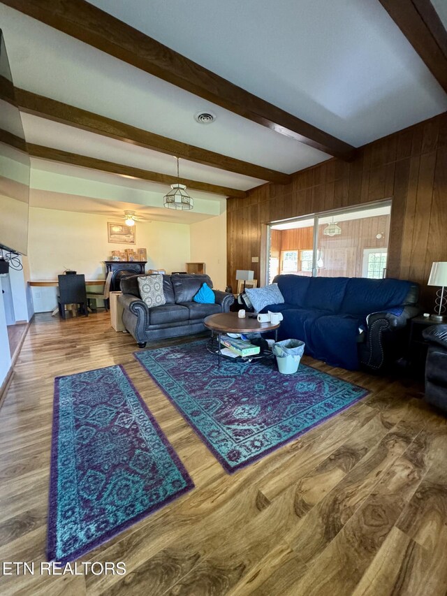 living area with visible vents, wood walls, beam ceiling, and wood finished floors