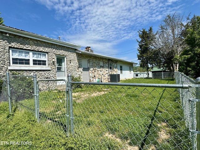 back of property featuring a chimney, a lawn, central air condition unit, fence, and stone siding