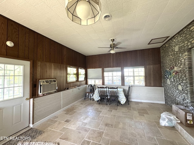 interior space featuring wooden walls, ceiling fan, stone tile floors, and a wealth of natural light