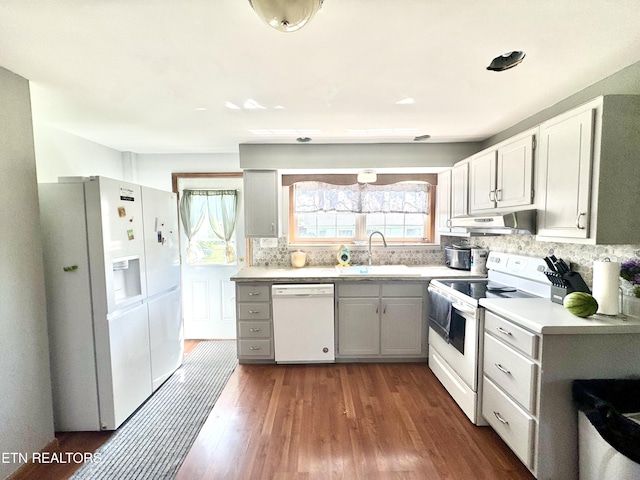 kitchen featuring white appliances, light countertops, under cabinet range hood, a sink, and dark wood finished floors
