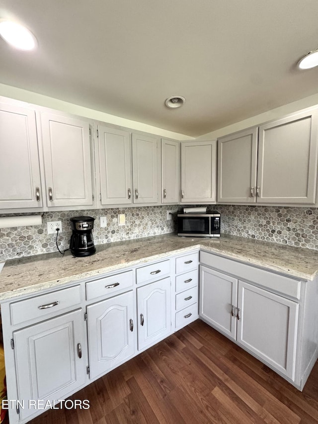kitchen featuring decorative backsplash, stainless steel microwave, dark wood-style floors, and light stone countertops