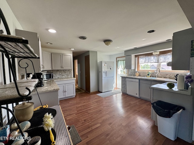 kitchen featuring a sink, dark wood-style flooring, backsplash, and white appliances