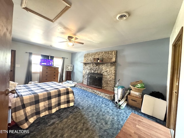bedroom with a fireplace, attic access, a ceiling fan, wood finished floors, and visible vents