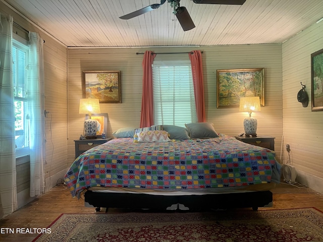 bedroom with multiple windows, wood walls, and wood finished floors