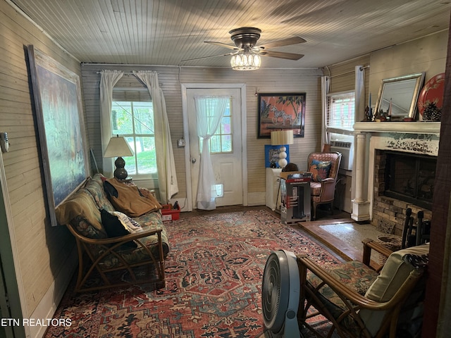 living area featuring a fireplace, ceiling fan, wood walls, and a healthy amount of sunlight