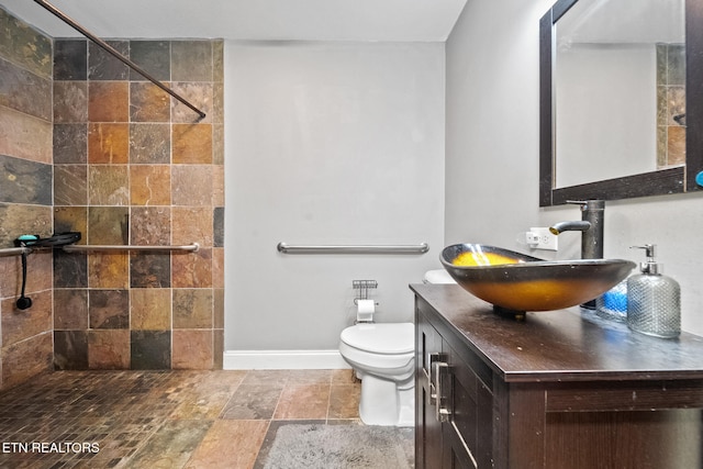 bathroom featuring vanity, baseboards, a tile shower, and toilet