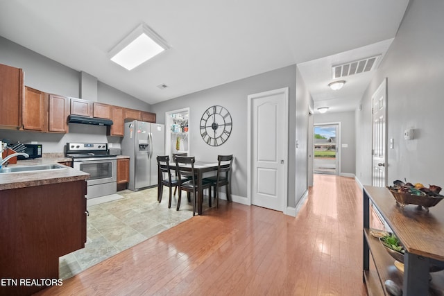 kitchen featuring visible vents, under cabinet range hood, a sink, appliances with stainless steel finishes, and vaulted ceiling