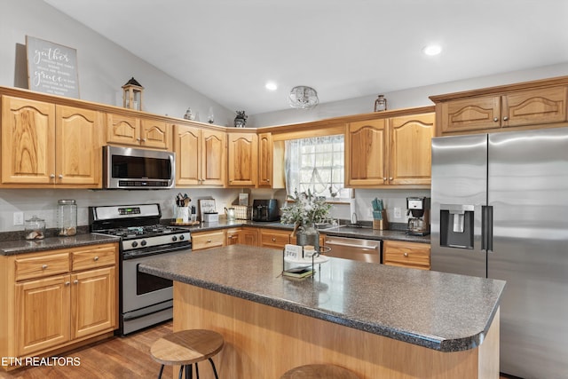kitchen with a kitchen bar, a center island, recessed lighting, vaulted ceiling, and stainless steel appliances