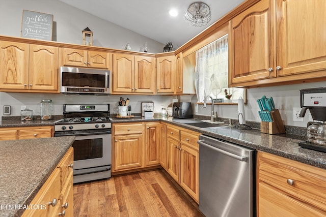 kitchen with a sink, light wood-style floors, dark stone counters, stainless steel appliances, and lofted ceiling