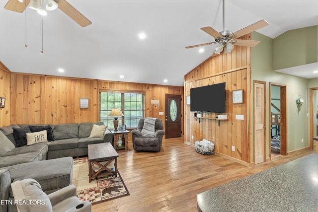 living room with vaulted ceiling, baseboards, a ceiling fan, and wood walls
