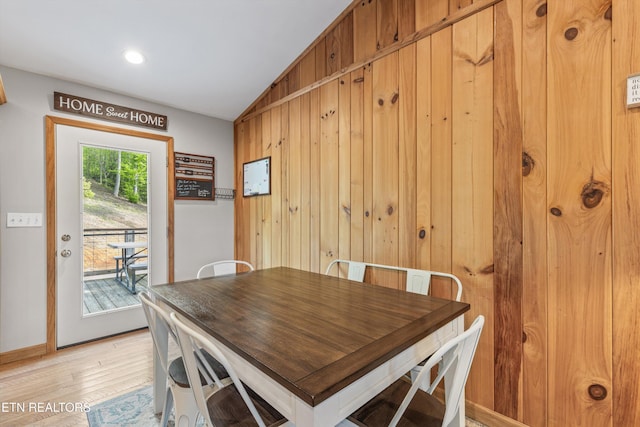 dining space featuring baseboards, wood walls, light wood-style flooring, and vaulted ceiling