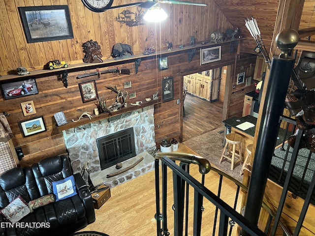 living area with wooden walls, a stone fireplace, and wood finished floors