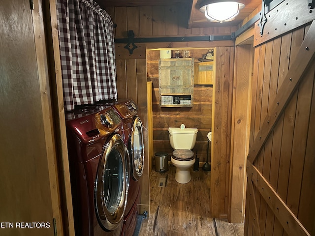 clothes washing area featuring wood finished floors, laundry area, a barn door, wood walls, and washer and clothes dryer