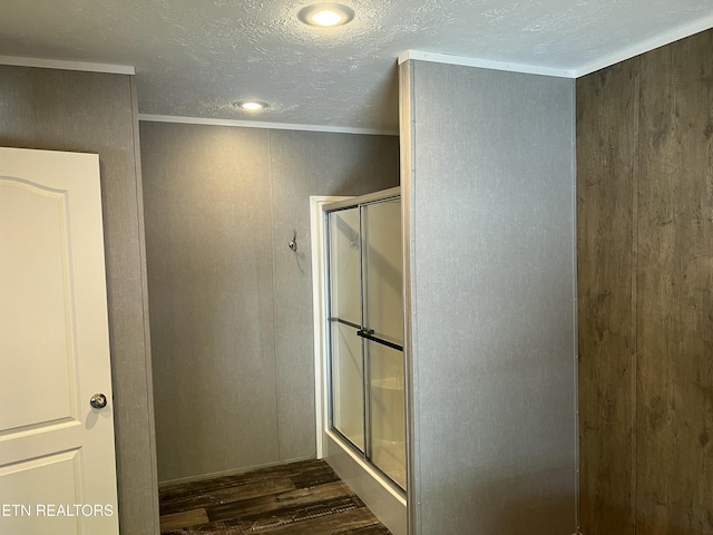 bathroom with a textured ceiling, wood finished floors, a shower stall, and crown molding