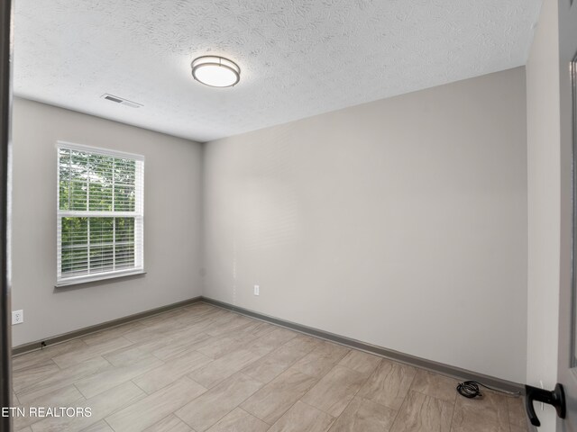 spare room featuring a textured ceiling, visible vents, and baseboards