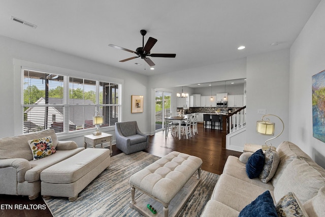living room featuring recessed lighting, ceiling fan with notable chandelier, visible vents, and dark wood-type flooring