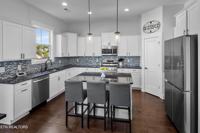 kitchen with white cabinetry, decorative backsplash, a sink, stainless steel appliances, and a kitchen island
