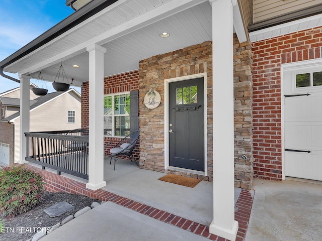 view of exterior entry with a porch, brick siding, and stone siding