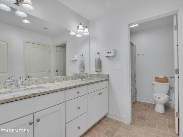 bathroom with baseboards, a sink, double vanity, and toilet