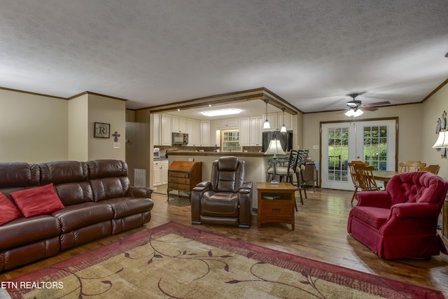 living area with visible vents, ornamental molding, wood finished floors, a textured ceiling, and a ceiling fan