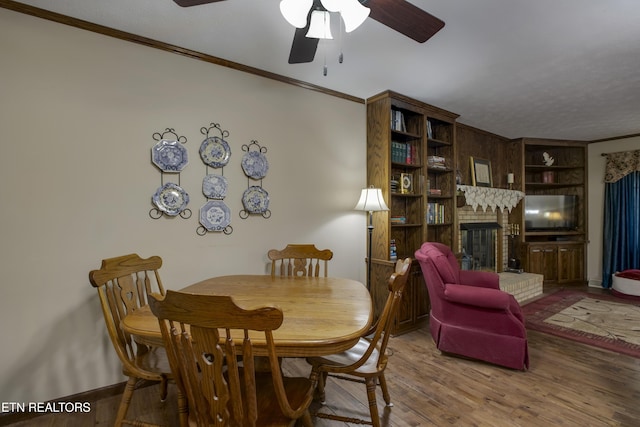 dining space featuring ornamental molding, a brick fireplace, wood finished floors, baseboards, and a ceiling fan