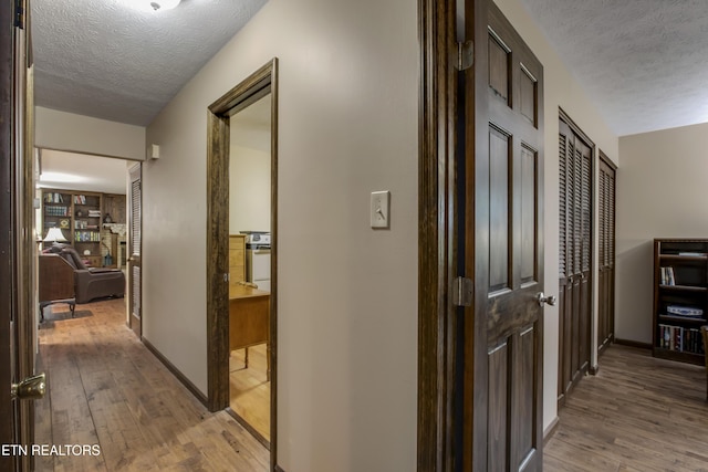hallway featuring a textured ceiling, baseboards, and light wood finished floors