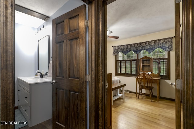 interior space featuring vanity, wood finished floors, baseboards, ceiling fan, and a textured ceiling