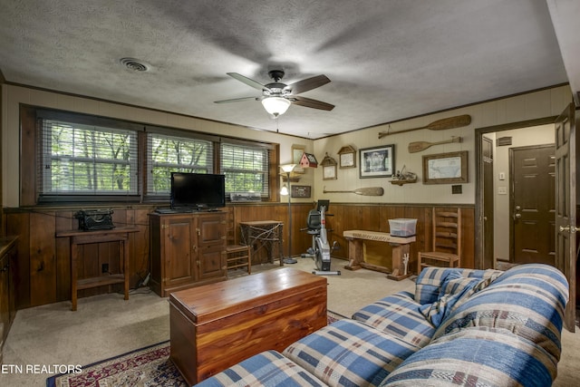 carpeted living area featuring a textured ceiling, ceiling fan, wood walls, and visible vents