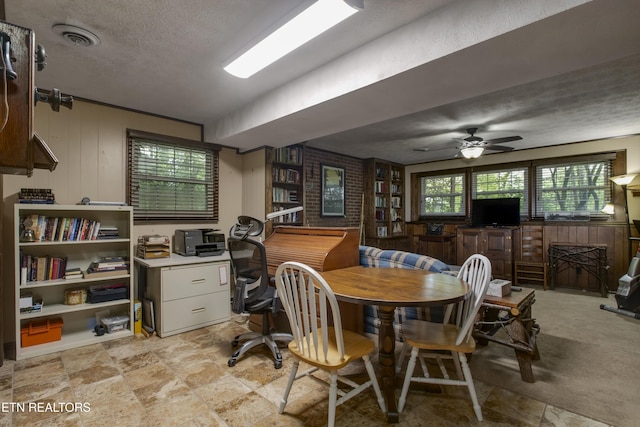 dining space featuring ceiling fan, wood walls, a textured ceiling, and visible vents