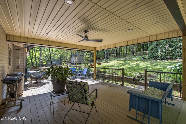 wooden deck with outdoor dining space, ceiling fan, and a yard