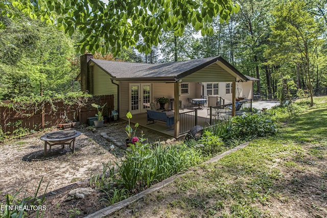 rear view of house with a fire pit, fence, french doors, a chimney, and a shingled roof