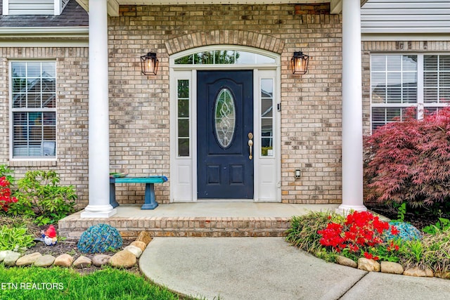 doorway to property featuring brick siding, a porch, and a shingled roof