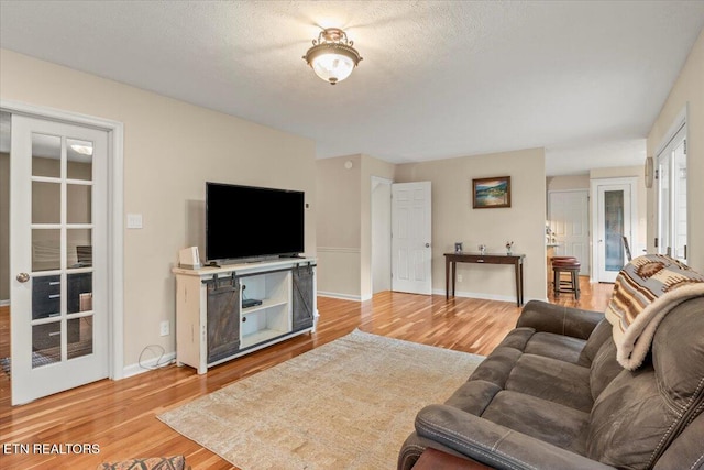 living area with a textured ceiling, baseboards, and light wood-type flooring