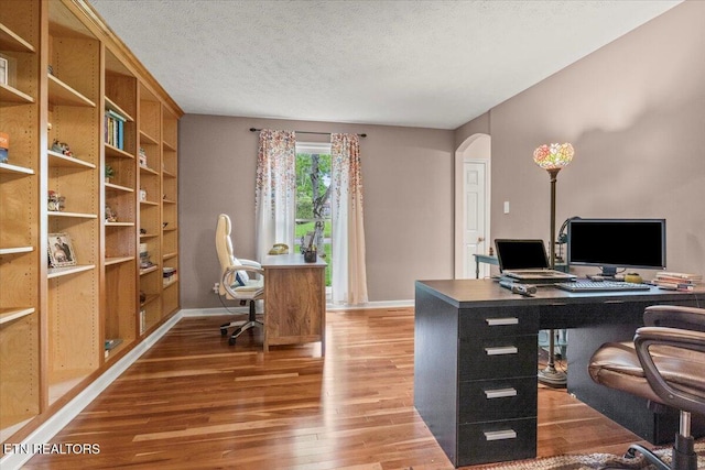 office area featuring arched walkways, a textured ceiling, wood finished floors, and baseboards