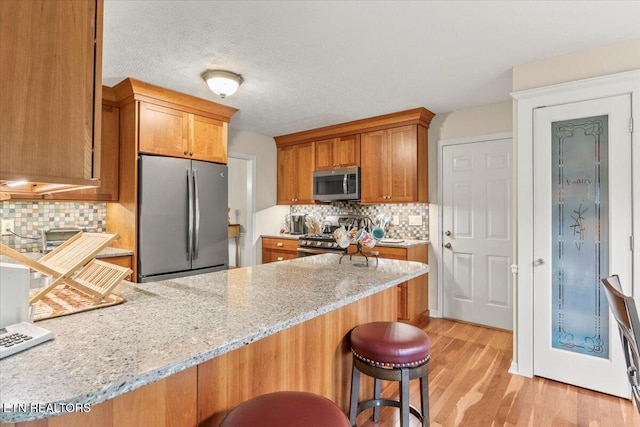 kitchen featuring light wood finished floors, a peninsula, appliances with stainless steel finishes, and tasteful backsplash