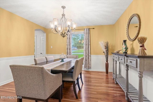 dining area featuring an inviting chandelier, wood finished floors, a wainscoted wall, and arched walkways