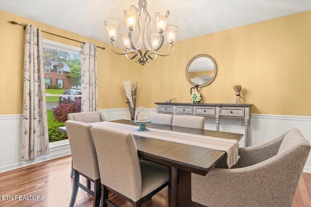 dining area featuring a chandelier, wood finished floors, and a wainscoted wall