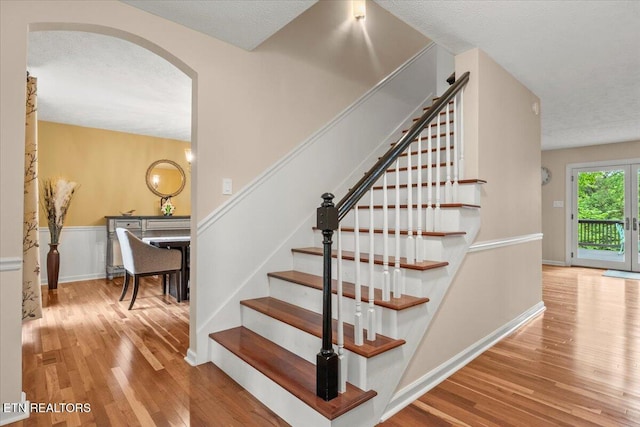 stairs featuring wood finished floors and arched walkways