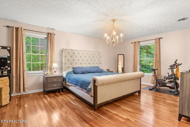 bedroom with a textured ceiling, visible vents, light wood-type flooring, and baseboards