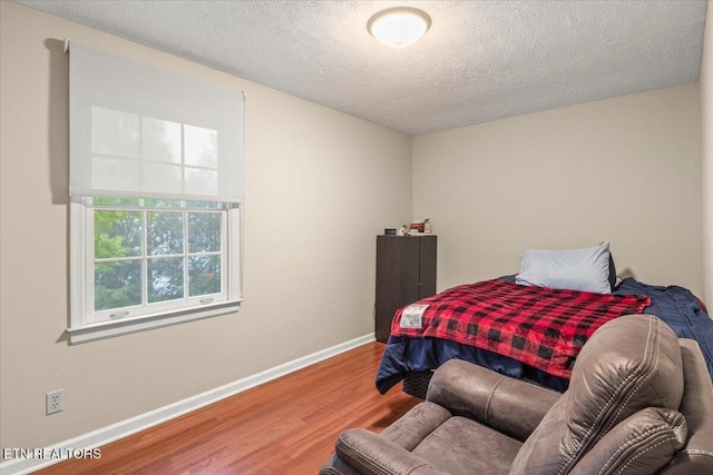 bedroom with baseboards, wood finished floors, and a textured ceiling