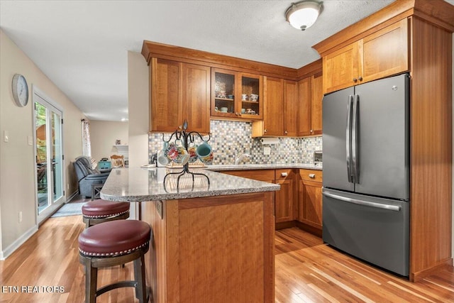 kitchen with tasteful backsplash, light stone counters, freestanding refrigerator, brown cabinetry, and light wood-style floors