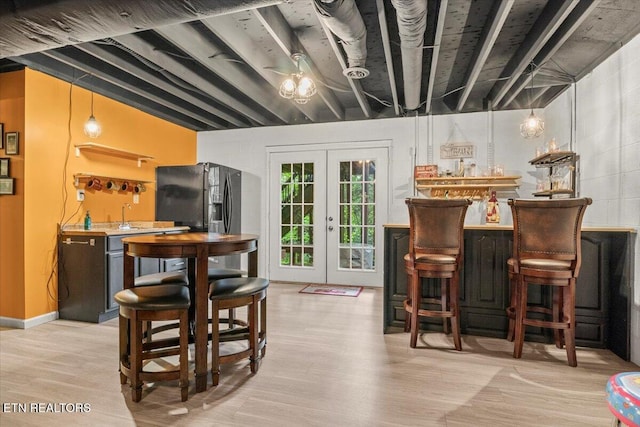 bar with black fridge with ice dispenser, light wood-style flooring, baseboards, indoor bar, and french doors