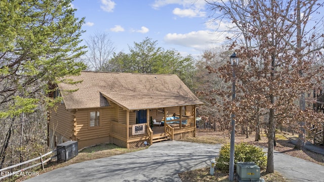 view of front facade with a porch, log siding, central air condition unit, aphalt driveway, and a shingled roof