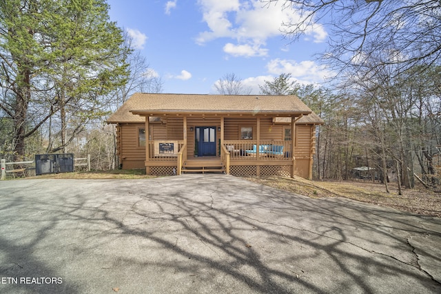 back of property with log siding, a shingled roof, and covered porch