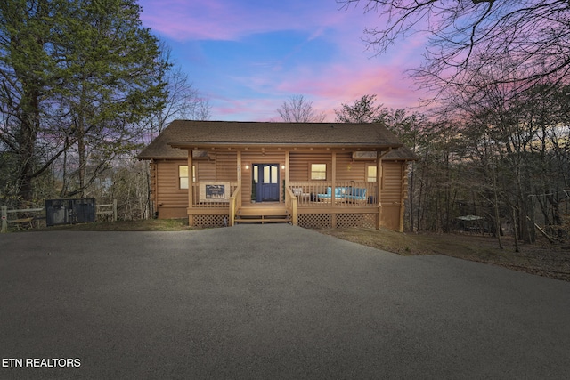 rustic home with roof with shingles, covered porch, and log siding