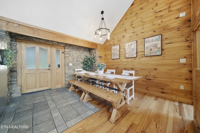 dining area featuring wood walls, wood finished floors, a chandelier, and high vaulted ceiling