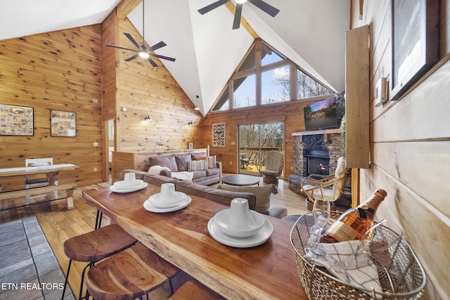 dining space featuring high vaulted ceiling, a ceiling fan, wood walls, and wood finished floors
